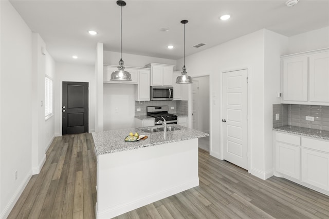 kitchen with hanging light fixtures, stainless steel appliances, an island with sink, and white cabinets