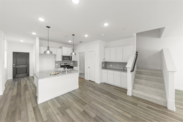 kitchen featuring white cabinetry, hanging light fixtures, stainless steel appliances, light stone countertops, and a kitchen island with sink