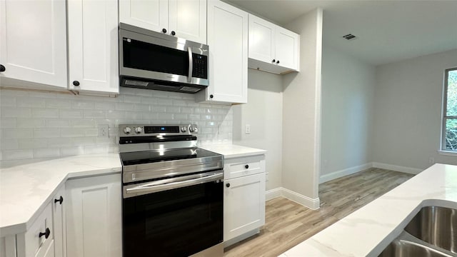 kitchen featuring decorative backsplash, light stone countertops, white cabinets, and appliances with stainless steel finishes