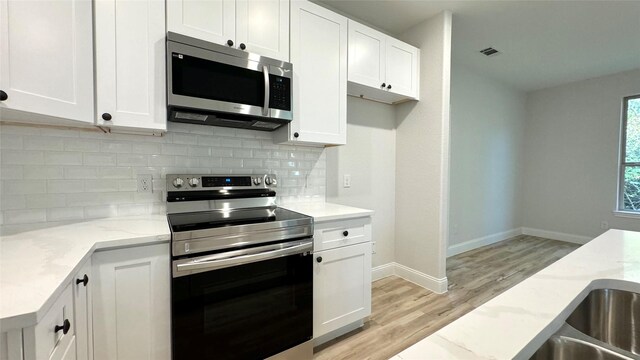 kitchen featuring appliances with stainless steel finishes, white cabinets, light stone counters, and decorative backsplash