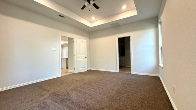 empty room with ceiling fan, dark carpet, and a raised ceiling