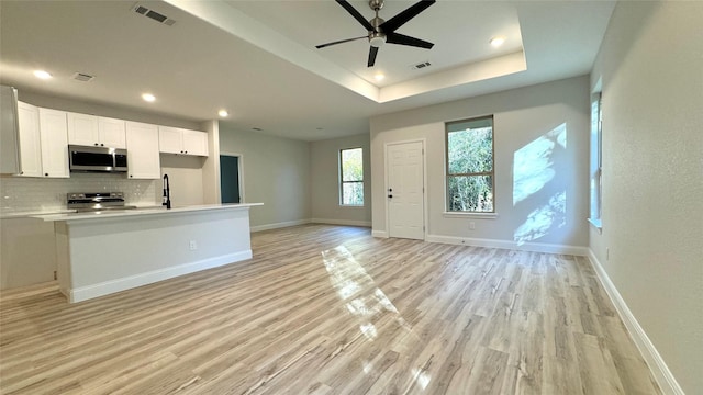 kitchen featuring a raised ceiling, light hardwood / wood-style flooring, decorative backsplash, white cabinets, and appliances with stainless steel finishes