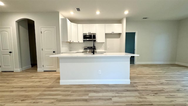 kitchen with white cabinets, light hardwood / wood-style floors, stainless steel appliances, and a kitchen island with sink