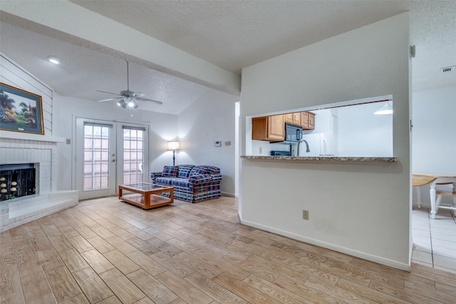 living room featuring french doors, a brick fireplace, a textured ceiling, vaulted ceiling, and ceiling fan