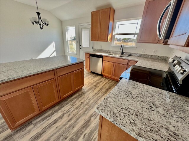 kitchen with appliances with stainless steel finishes, vaulted ceiling, sink, pendant lighting, and light hardwood / wood-style floors