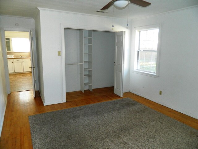 unfurnished bedroom with a closet, ceiling fan, crown molding, and wood-type flooring