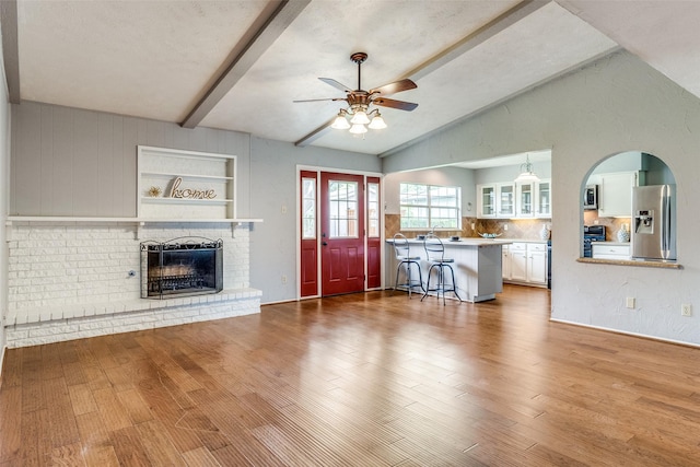 unfurnished living room featuring hardwood / wood-style flooring, vaulted ceiling with beams, ceiling fan, a fireplace, and a textured ceiling