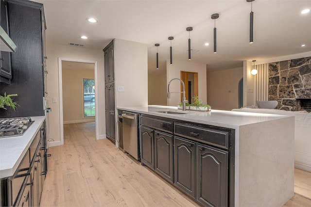 kitchen featuring a kitchen island with sink, hanging light fixtures, sink, light hardwood / wood-style flooring, and appliances with stainless steel finishes