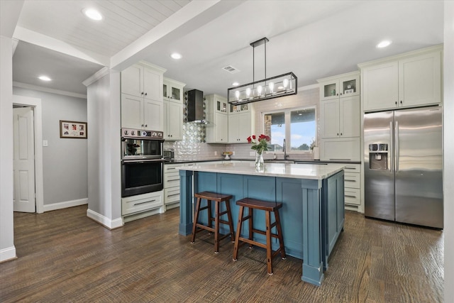 kitchen with a center island, dark wood-type flooring, wall chimney range hood, appliances with stainless steel finishes, and decorative light fixtures