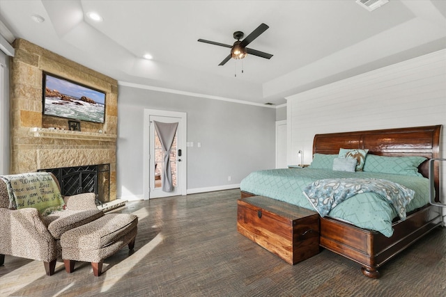 bedroom featuring ceiling fan, a stone fireplace, dark wood-type flooring, and a tray ceiling