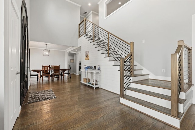 stairway with crown molding, a towering ceiling, wood-type flooring, and an inviting chandelier