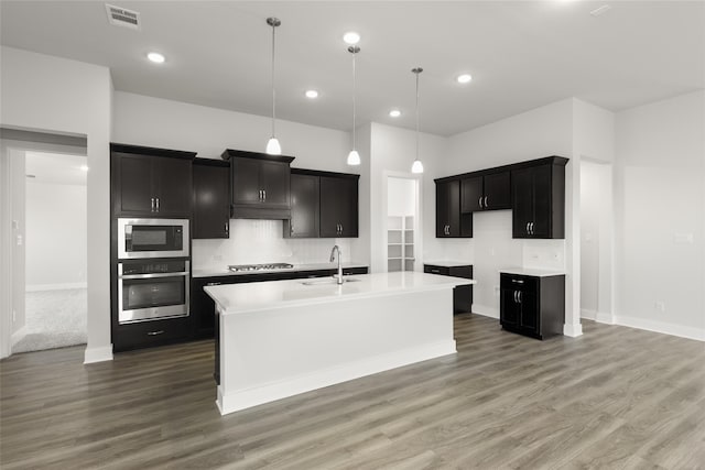 kitchen featuring an island with sink, appliances with stainless steel finishes, sink, and decorative light fixtures