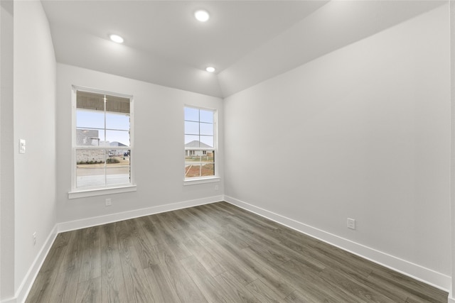 spare room featuring wood-type flooring and vaulted ceiling