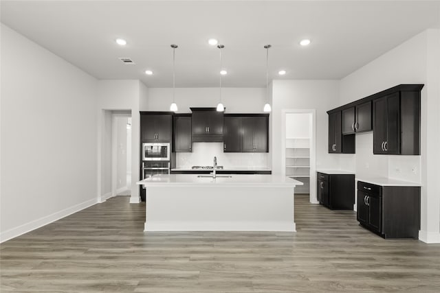 kitchen featuring an island with sink, appliances with stainless steel finishes, light hardwood / wood-style flooring, and decorative light fixtures