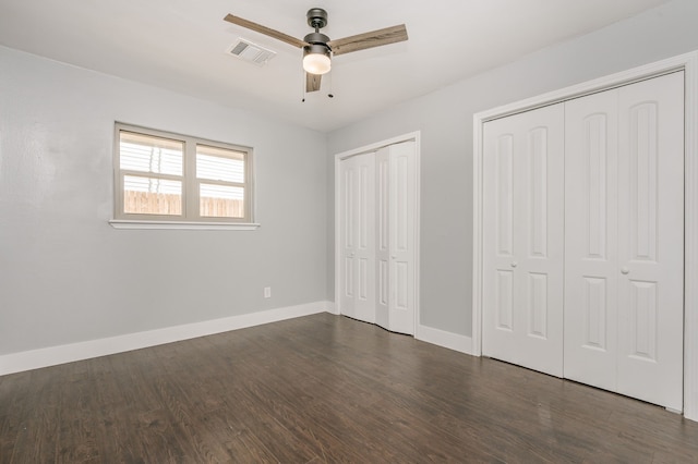 unfurnished bedroom with multiple closets, dark wood-type flooring, and ceiling fan
