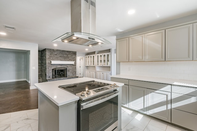 kitchen featuring island range hood, electric range, gray cabinets, a fireplace, and decorative backsplash