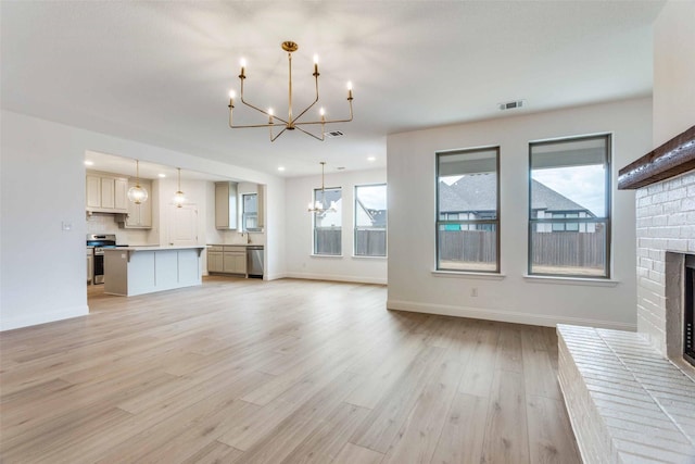 unfurnished living room with light wood-type flooring, a brick fireplace, a wealth of natural light, and a notable chandelier