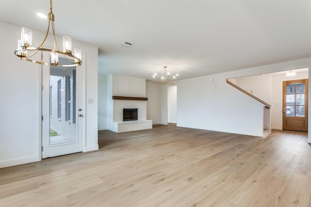 unfurnished living room featuring visible vents, light wood-style floors, a brick fireplace, a chandelier, and baseboards