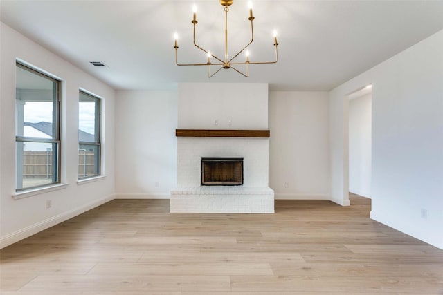 unfurnished living room featuring a notable chandelier, visible vents, baseboards, light wood-type flooring, and a brick fireplace