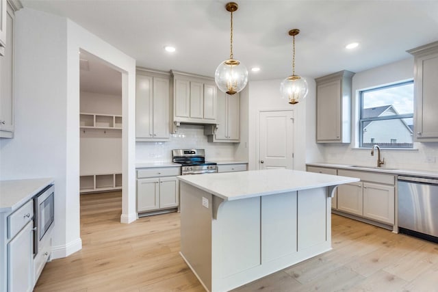 kitchen with light wood-type flooring, a kitchen island, appliances with stainless steel finishes, and a sink