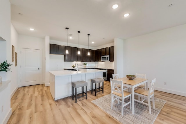 kitchen featuring a kitchen island with sink, sink, pendant lighting, and light hardwood / wood-style floors