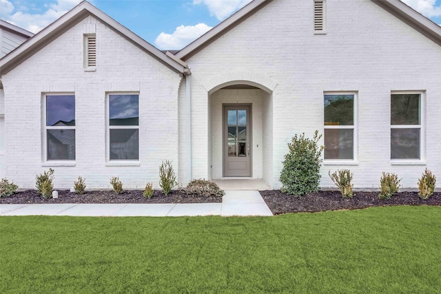 doorway to property featuring a lawn and brick siding