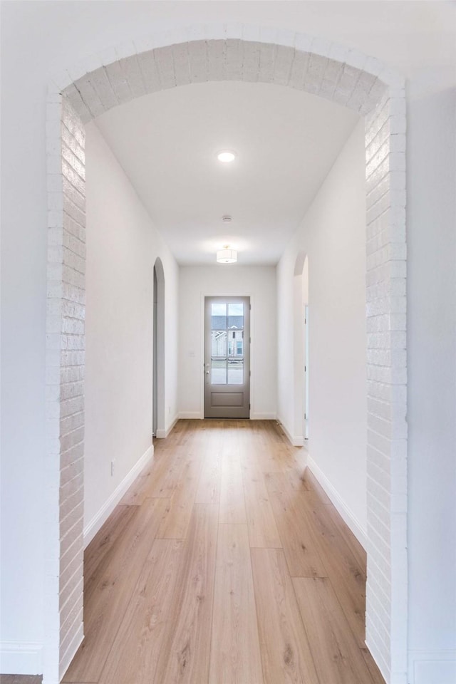 hall with arched walkways, light wood-style flooring, and baseboards