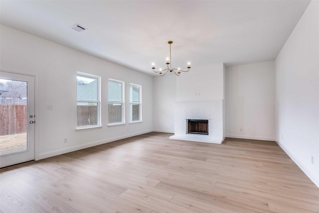 unfurnished living room featuring baseboards, a fireplace, an inviting chandelier, and light wood-style floors