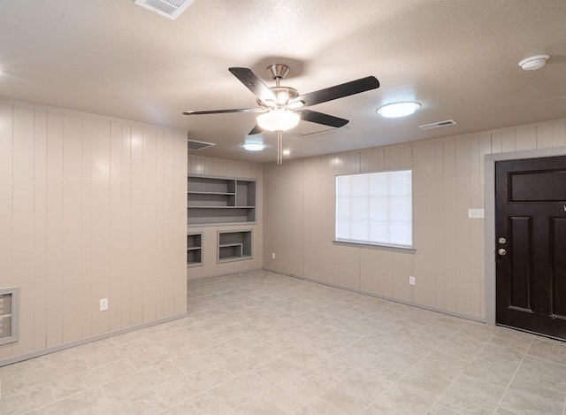 unfurnished living room featuring a textured ceiling, ceiling fan, and wood walls