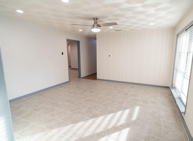 unfurnished room featuring ceiling fan, wooden walls, and light tile patterned flooring