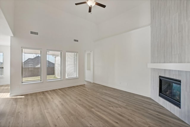 unfurnished living room with hardwood / wood-style flooring, ceiling fan, a fireplace, and high vaulted ceiling