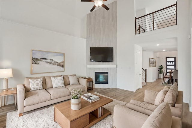 living room featuring ceiling fan, a large fireplace, a towering ceiling, and light hardwood / wood-style flooring