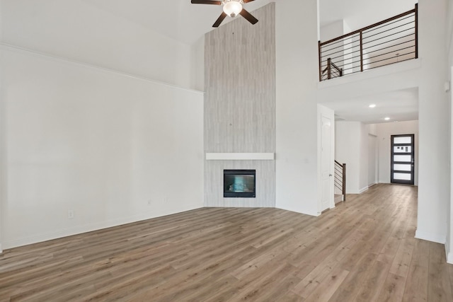 unfurnished living room with a fireplace, wood-type flooring, ceiling fan, and a high ceiling