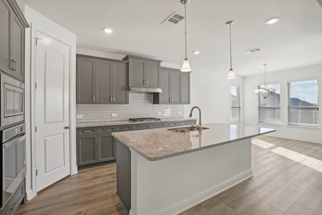 kitchen featuring hardwood / wood-style floors, light stone countertops, sink, and stainless steel appliances