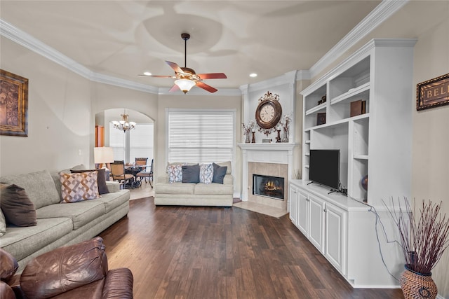 living room featuring a fireplace, ceiling fan with notable chandelier, dark hardwood / wood-style floors, and crown molding