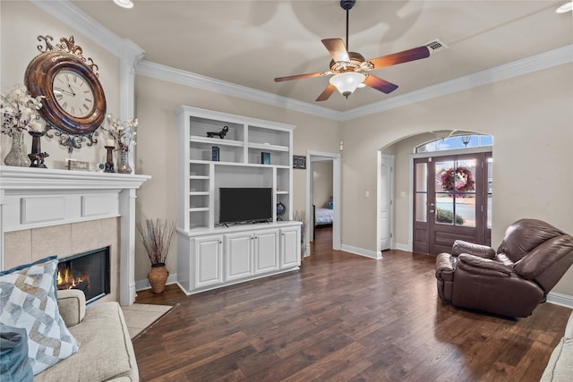 living room with dark hardwood / wood-style floors, ceiling fan, crown molding, and a tiled fireplace