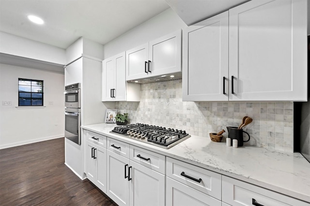 kitchen with white cabinetry, appliances with stainless steel finishes, dark hardwood / wood-style floors, light stone countertops, and decorative backsplash