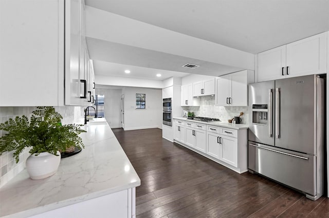 kitchen with light stone counters, white cabinets, dark hardwood / wood-style floors, and appliances with stainless steel finishes