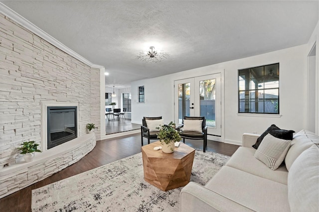 living room featuring a stone fireplace, hardwood / wood-style floors, ornamental molding, a textured ceiling, and french doors