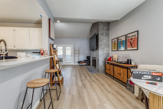 kitchen featuring a tile fireplace, white cabinetry, french doors, a kitchen breakfast bar, and light wood-type flooring