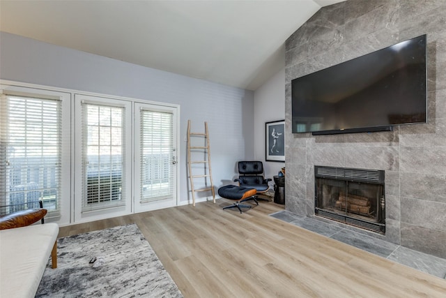 living room featuring hardwood / wood-style flooring, lofted ceiling, and a tiled fireplace