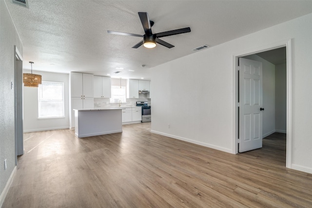 unfurnished living room with ceiling fan, light hardwood / wood-style floors, sink, and a textured ceiling