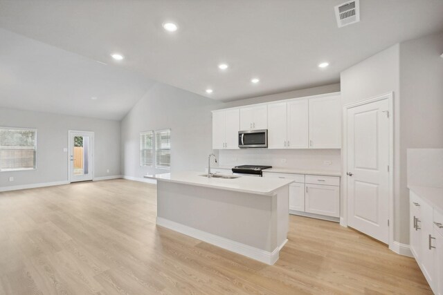 kitchen with appliances with stainless steel finishes, light wood-type flooring, a kitchen island with sink, sink, and lofted ceiling