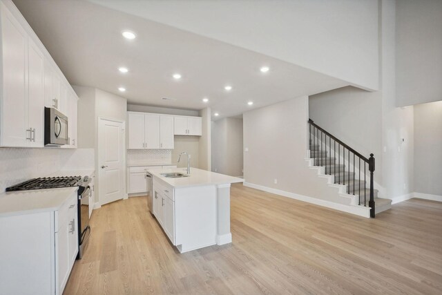 kitchen featuring a center island with sink, white cabinets, sink, light hardwood / wood-style flooring, and appliances with stainless steel finishes