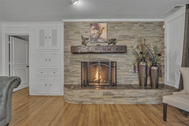 living room with light hardwood / wood-style flooring, a stone fireplace, and ornamental molding