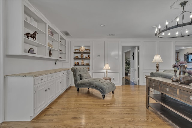 sitting room with a chandelier, built in shelves, light wood-type flooring, and crown molding