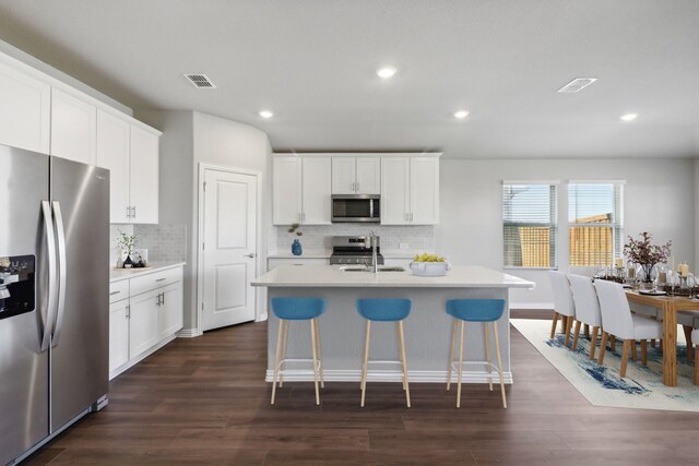 kitchen with stainless steel appliances, a kitchen island with sink, and dark wood-type flooring