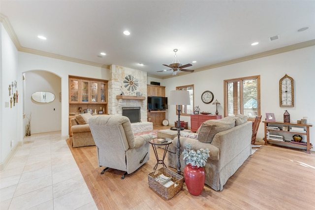 living room featuring a stone fireplace, ornamental molding, ceiling fan, and light wood-type flooring