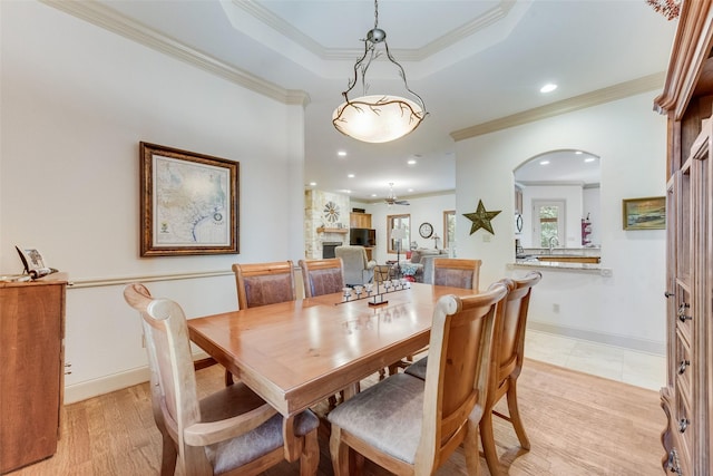 dining space featuring ceiling fan, sink, light hardwood / wood-style floors, a fireplace, and ornamental molding