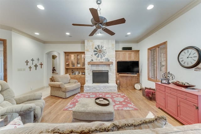 living room featuring a stone fireplace, crown molding, light hardwood / wood-style flooring, and ceiling fan